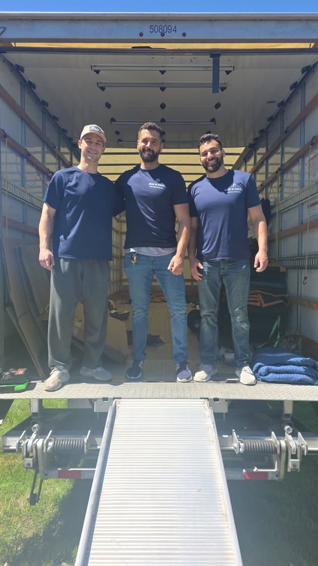 Three smiling Box N Haul movers standing together on the truck ramp after a move.